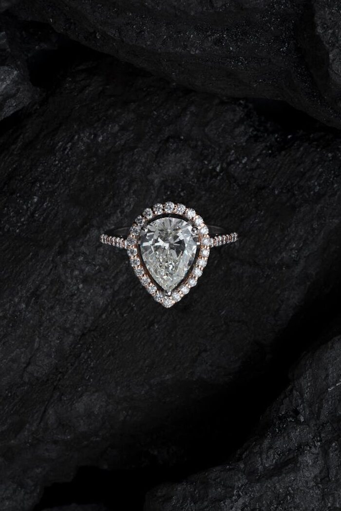 Stunning teardrop diamond ring surrounded by smaller stones on a textured dark background.
