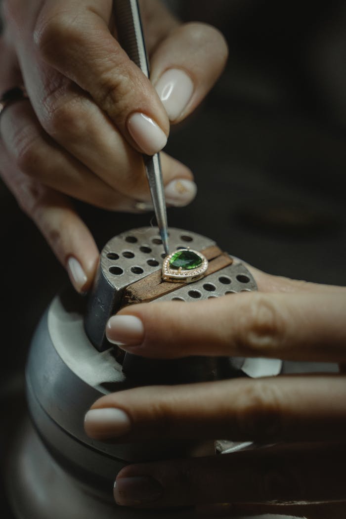 About A skilled jeweler carefully crafting an emerald ring using a tweezer, showcasing craftsmanship.